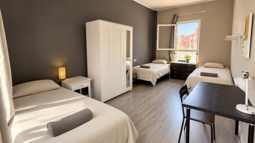 Shared room at Banama Coliving hostel in Corralejo with multiple beds, desk, wardrobe, and window view