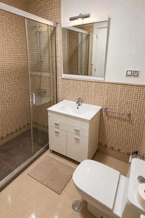 Modern bathroom in Banama Coliving hostel, Corralejo with tiled shower, white vanity sink, toilet, and mirror