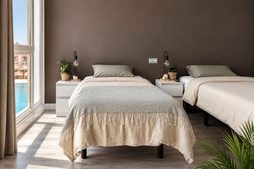 Modern twin bedroom at Banama Coliving hostel in Corralejo with beige bedding, white nightstands, pool view window, and