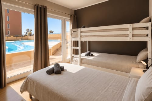 Bright dorm room at Banama Coliving in Corralejo with bunk beds, balcony overlooking swimming pool