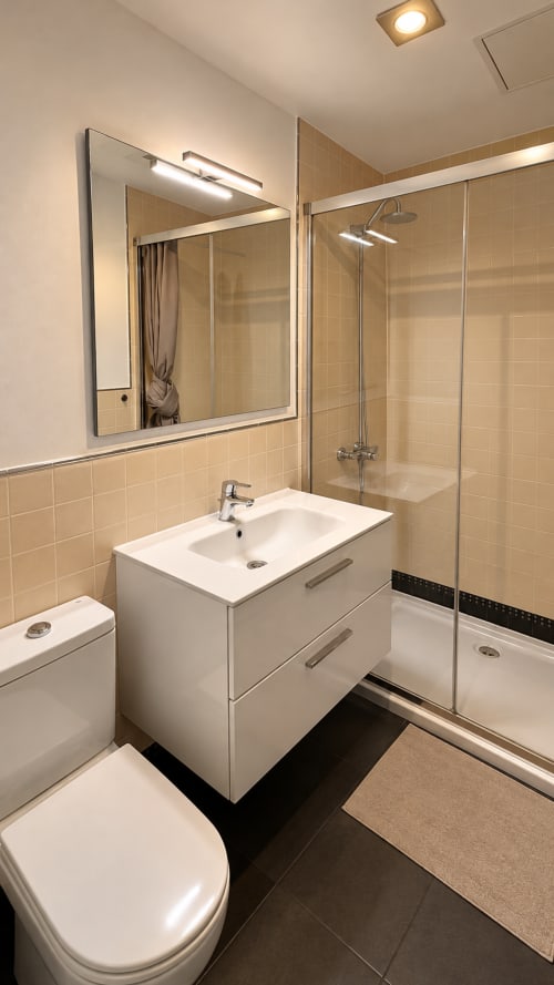 Modern bathroom in Banama Coliving hostel, Corralejo with white vanity, mirrored cabinet, and glass shower enclosure