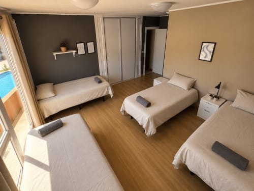 Shared 4-person dorm room at Banama Coliving hostel in Corralejo with four beds, wooden floors, and pool view balcony