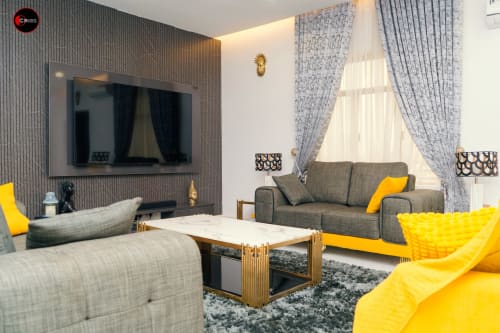 Modern CASA OD apartment at OD Cribs Abuja with gray sofas, yellow accents, flat-screen TV, and elegant furnishings