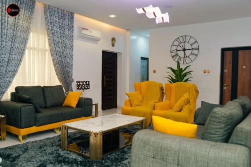 Modern sitting area at OD Cribs Abuja with yellow and gray armchairs, marble table, and large windows
