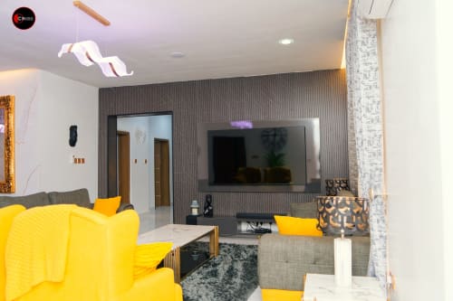Modern living room at OD Cribs CASA apartment in Abuja with yellow sofa, flat-screen TV, and stylish decor