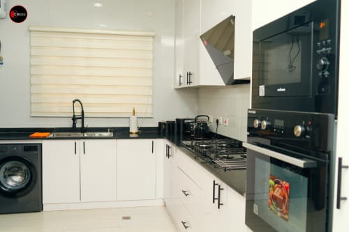 Modern kitchen at OD Cribs apartment in Abuja with white cabinets, black countertops, gas stove, and built-in black