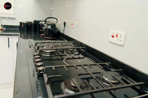 Modern kitchen setup at OD Cribs CASA in Abuja with gas cooktop, black countertop, kettle, and white wall outlets