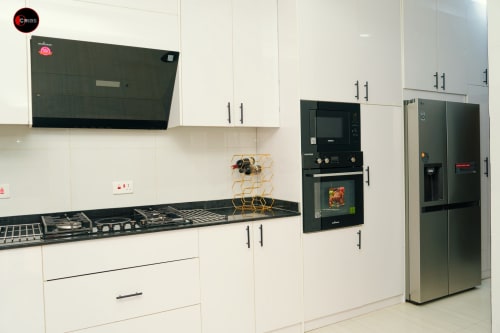 Modern kitchen at OD Cribs CASA apartment in Abuja with white cabinetry, black appliances, gas cooktop, and stainless steel