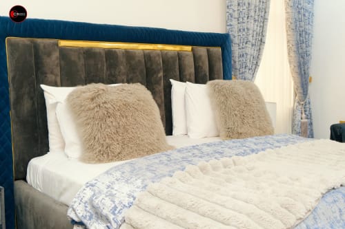 Luxury bedroom at OD Cribs Abuja with blue upholstered headboard, beige pillows, and white bedding