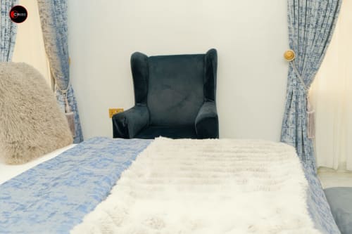 CASA OD apartment bedroom at OD Cribs Abuja with blue-patterned curtains, white bedding, and dark armchair sitting area