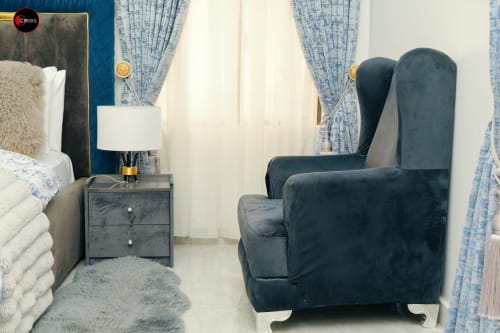 Elegant CASA OD bedroom at OD Cribs Abuja featuring blue velvet armchair, dark nightstand with lamp, and blue patterned