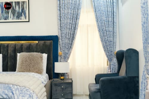 Luxury bedroom at OD Cribs Abuja with blue velvet bed, tufted headboard, blue patterned curtains, and seating area