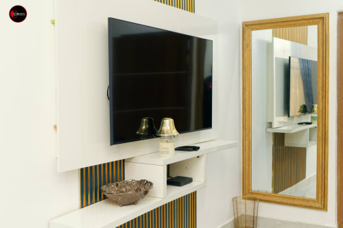 Modern hotel room at OD Cribs Abuja featuring wall-mounted flat screen TV, white desk with gold accents, and large mirror