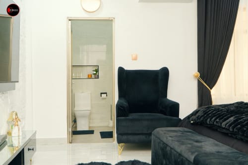 Modern bedroom at OD Cribs CASA apartment in Abuja with black velvet chair, bed, and ensuite bathroom visible through glass