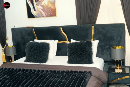 Luxury bedroom at OD Cribs Abuja with dark teal headboard, white bedding, black fur pillows, and gold accents