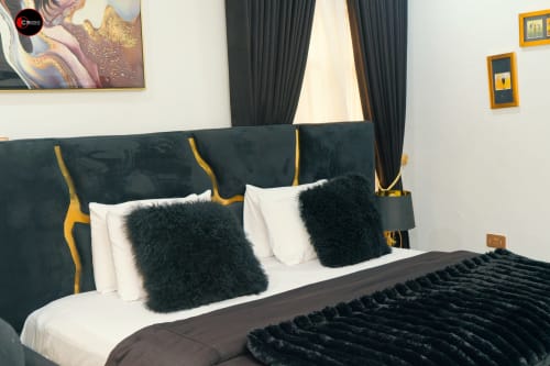 Luxurious bedroom at OD Cribs Abuja featuring teal velvet headboard with gold accents, white pillows, black fur cushions, and
