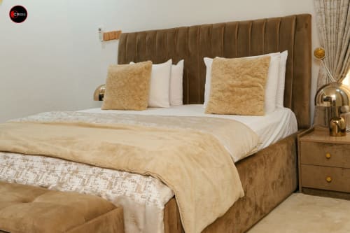 Luxurious bedroom at OD Cribs hotel in Abuja with tan upholstered headboard, white bedding, gold pillows, and modern