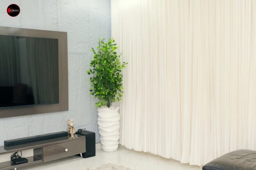 Modern living room at OD Cribs Abuja with wall-mounted TV, white textured vase with greenery, and cream curtains