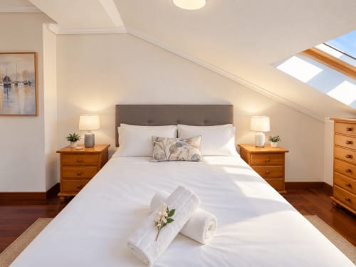 Luminoso dormitorio en desván con vistas al mar, muebles de madera, ropa de cama blanca y claraboya en apartamento Holibai, Baiona