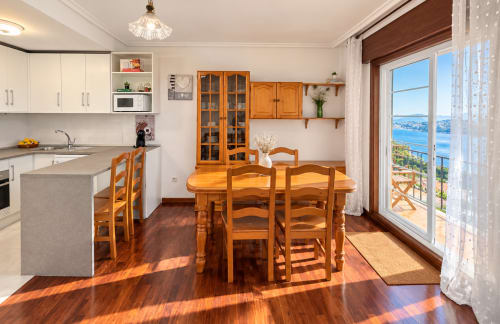 Comedor luminoso con muebles de madera y balcón con vistas al mar en apartamento de Baiona