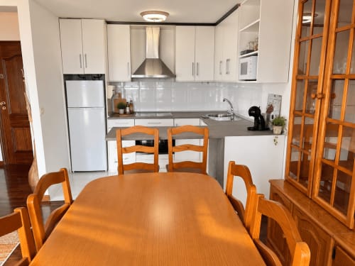 Cocina y comedor moderno en apartamento de Baiona con gabinetes blancos, electrodomésticos de acero inoxidable y muebles de madera