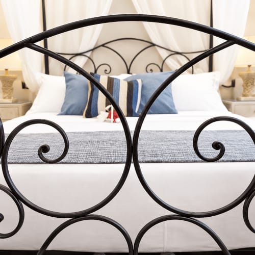 Letto in ferro battuto nero con cuscini rigati blu e bianco, biancheria bianca e tende beige nella camera Gli Amanti della B&B