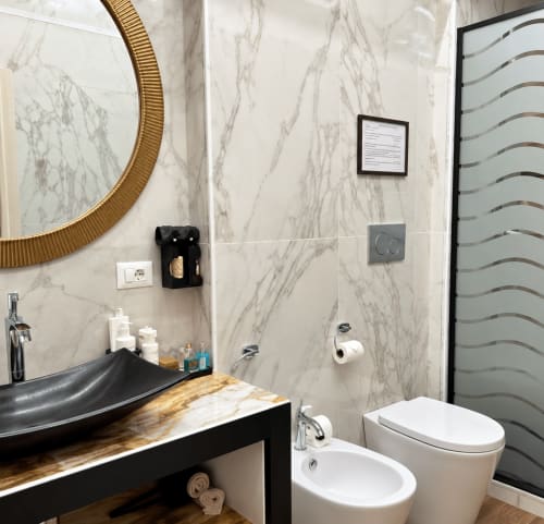 Bagno moderno del B&B I Mori a Catania con lavabo nero, muri in marmo, specchio dorato e bidet