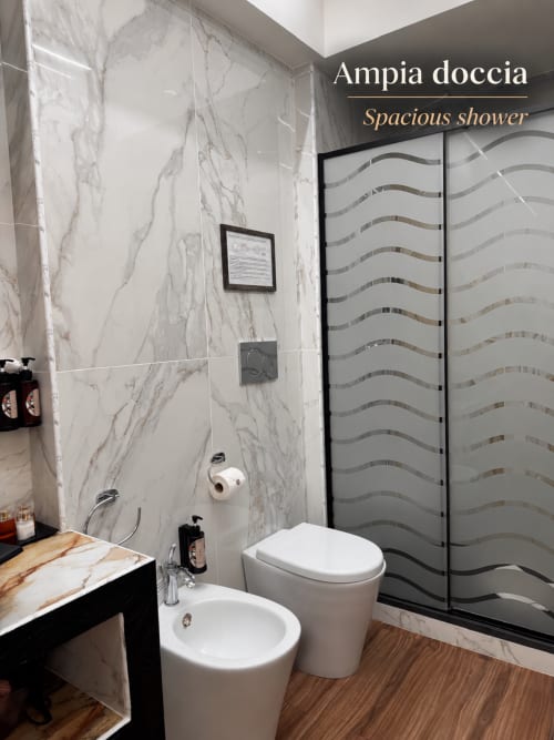 Bagno moderno della B&B I Mori Catania con piastrelle effetto marmo, spaziosa doccia, sanitari bianchi e pavimento in legno