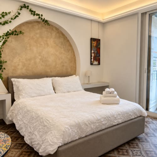 Quarto elegante no B&B I Mori Catania com cabeceira em arco, roupa de cama branca, varanda com vista para a cidade e comodidades modernas
