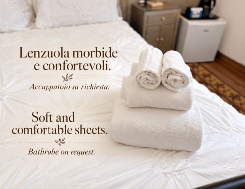 Toalhas e roupas de cama brancas enroladas na cama do B&B I Mori Catania, com texto de amenidades em italiano e inglês