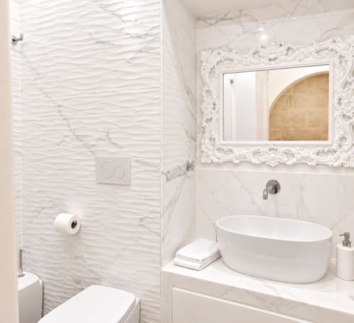 Banheiro moderno da B&B I Mori Catania com azulejos de mármore, pia branca, espelho ornamentado e área de chuveiro