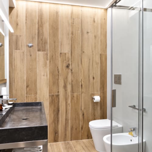 Nowoczesna łazienka w B&B I Mori Catania z płytkami imitującymi drewno, czarną umywalką, białą toaletą i przesuwną kabinę prysznicową ze szkła