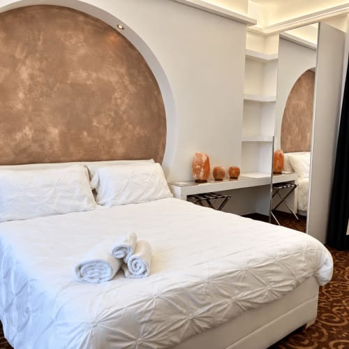 Dormitorio moderno en B&B I Mori Catania con cabecero arqueado, ropa de cama blanca, toallas enrolladas y tocador espejado con lámparas de sal