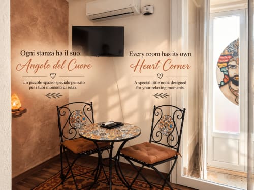 Rincón acogedor en el B&B I Mori de Catania con texto decorativo en la pared, mesita, dos sillas ornamentales y TV