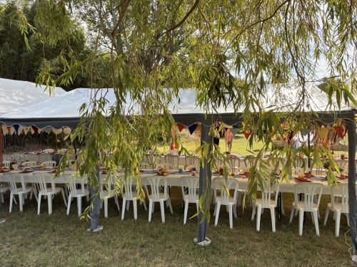 Outdoor wedding reception under tent with white chairs and willow tree at Les Jardins Du Soleil, Avignon