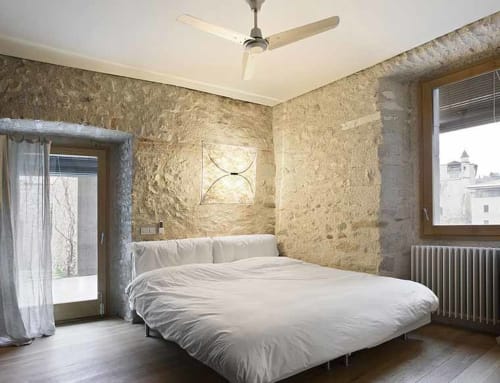 Modern bedroom at Alemanys 5 B&B in Girona with stone walls, white bed, and ceiling fan