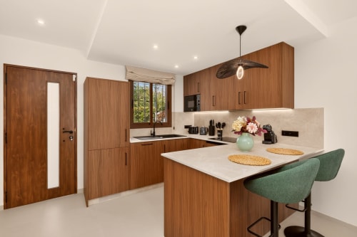 Cocina de lujo moderna con muebles de madera, encimeras blancas, isla con asientos y vistas al mar en villa de Nerja