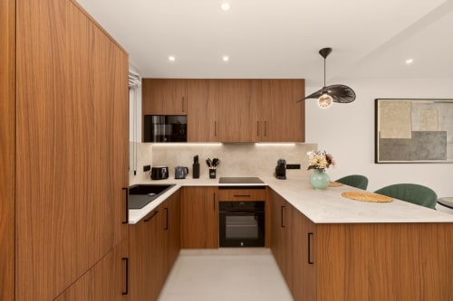 Cocina moderna con muebles de madera clara, encimeras blancas y electrodomésticos negros en Villa Mandarinos, casa de lujo en Nerja
