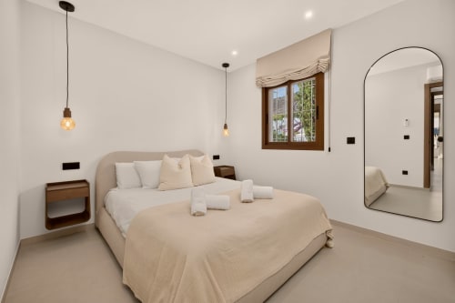 Dormitorio de lujo moderno en villa Nerja Holiday Home con muebles beige, iluminación colgante, espejo arqueado y vistas al mar