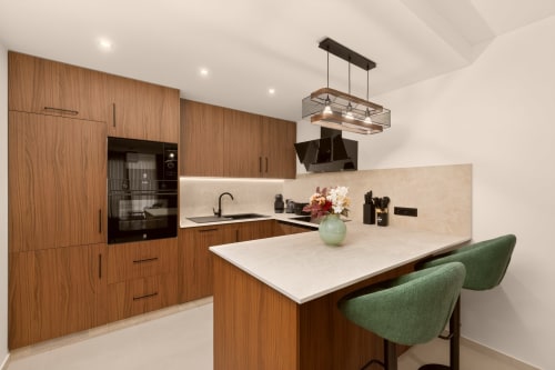 Cocina moderna con muebles de madera, isla con encimera blanca, sillas verdes e iluminación colgante en Villa Mandarinos, Nerja