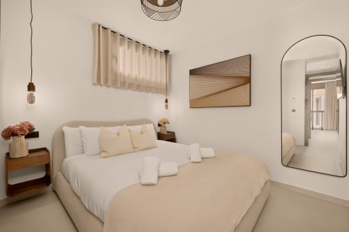 Lujosa villa en Nerja, dormitorio con cama beige, mesilla de madera, lámparas colgantes y espejo arqueado