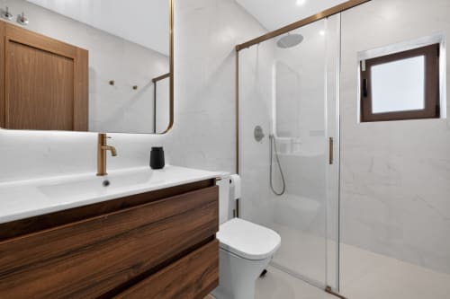 Baño de lujo moderno en villa de Nerja con baldosas de mármol, tocador de madera, accesorios de bronce y ducha a ras de suelo