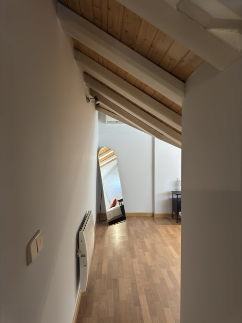 Luminoso apartamento tipo loft en Madrid con vigas de madera, suelos de parquet y espejo de cuerpo entero reflejando luz natural