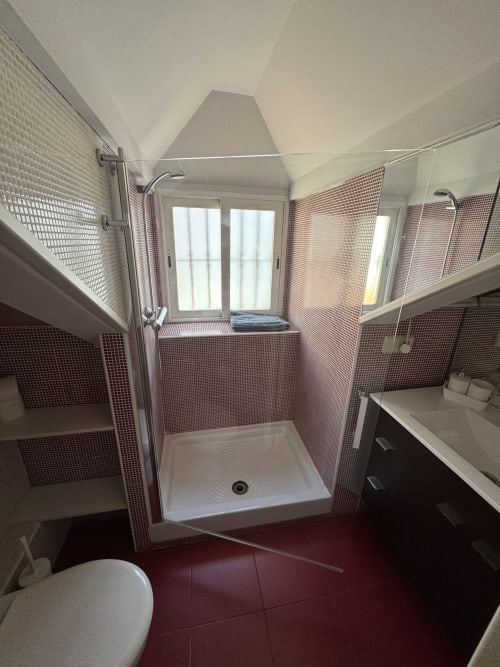 Baño moderno de apartamento madrileño con suelo de baldosas rojas, paredes con mosaicos rosa, ducha abierta, lavabo y ventana con vistas a la ciudad