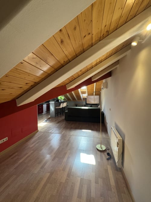 Moderno ático en Madrid con vigas de madera, pared roja de acento, zona de cocina y suelos de madera natural