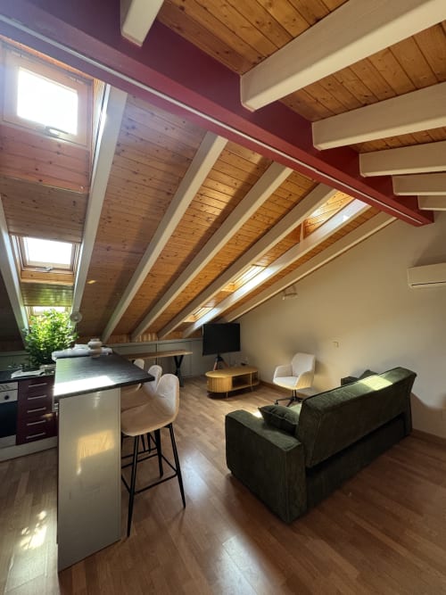 Acogedor ático moderno en Madrid con vigas de madera, isla de cocina, sofá oscuro y tragaluces con luz natural y vistas a la ciudad