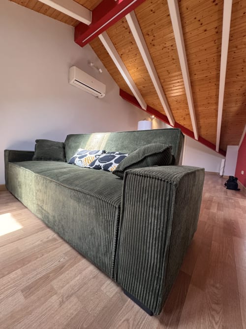 Sofá de pana gris moderno en ático madrileño con vigas de madera y detalles rojos, vistas a la ciudad
