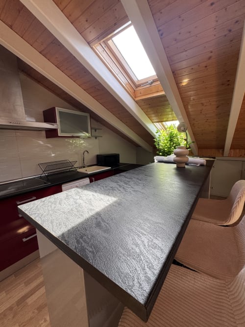 Moderna cocina abuhardillada con claraboya, encimeras grises, armarios rojos y techo de madera en apartamento madrileño