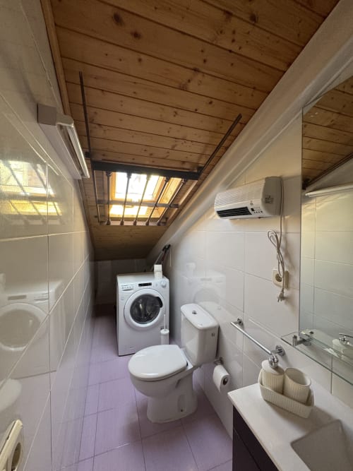 Baño moderno con lavadora, inodoro, lavamanos y claraboya en apartamento de Madrid