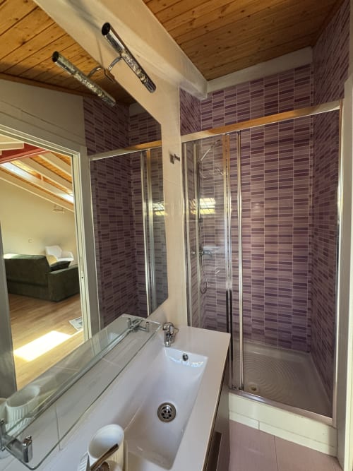 Baño moderno con ducha de azulejos púrpura, lavabo blanco y espejo en apartamento madrileño con vistas a la ciudad